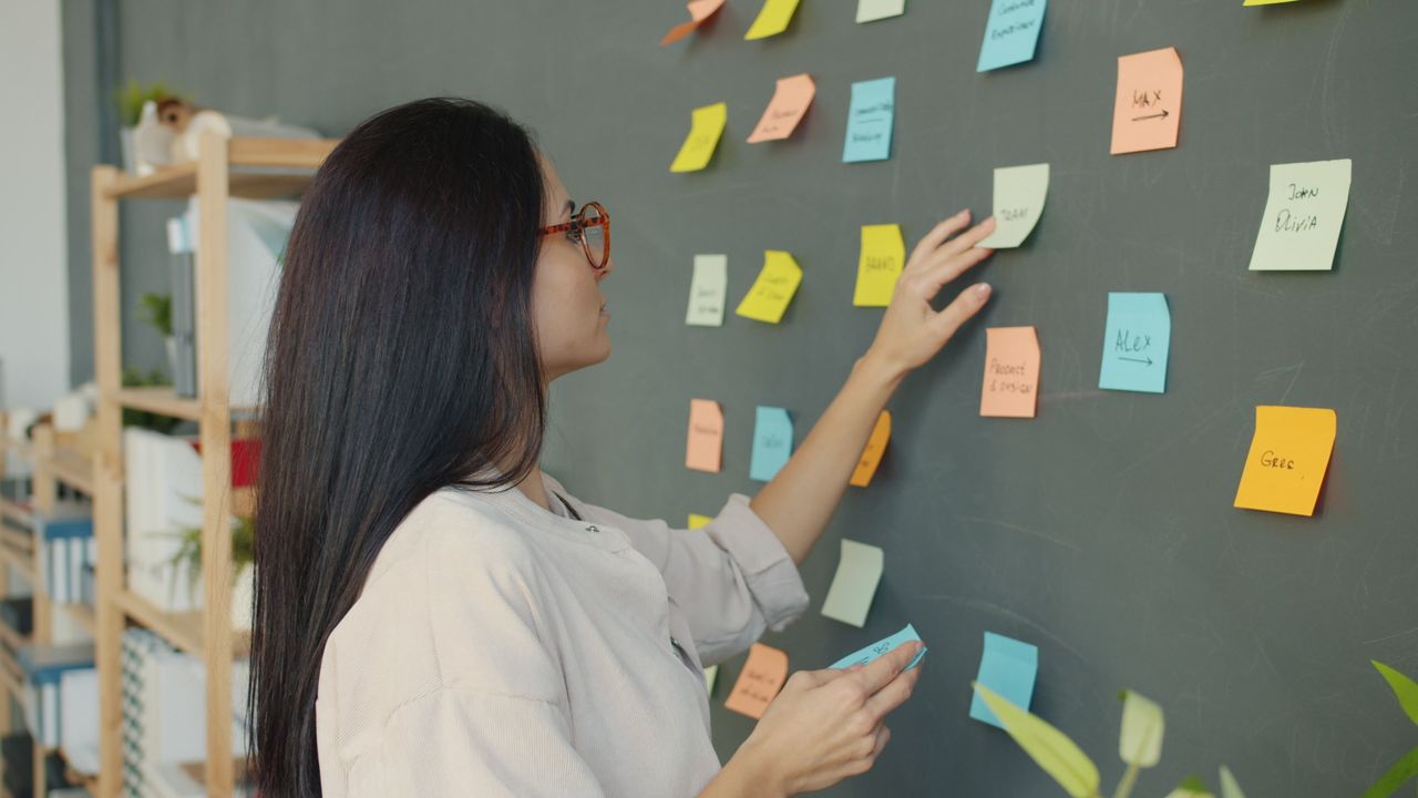 The Art of Drawing Readers In: Your attractive post title goes here Woman placing colorful sticky notes on a blackboard in a modern office setting.